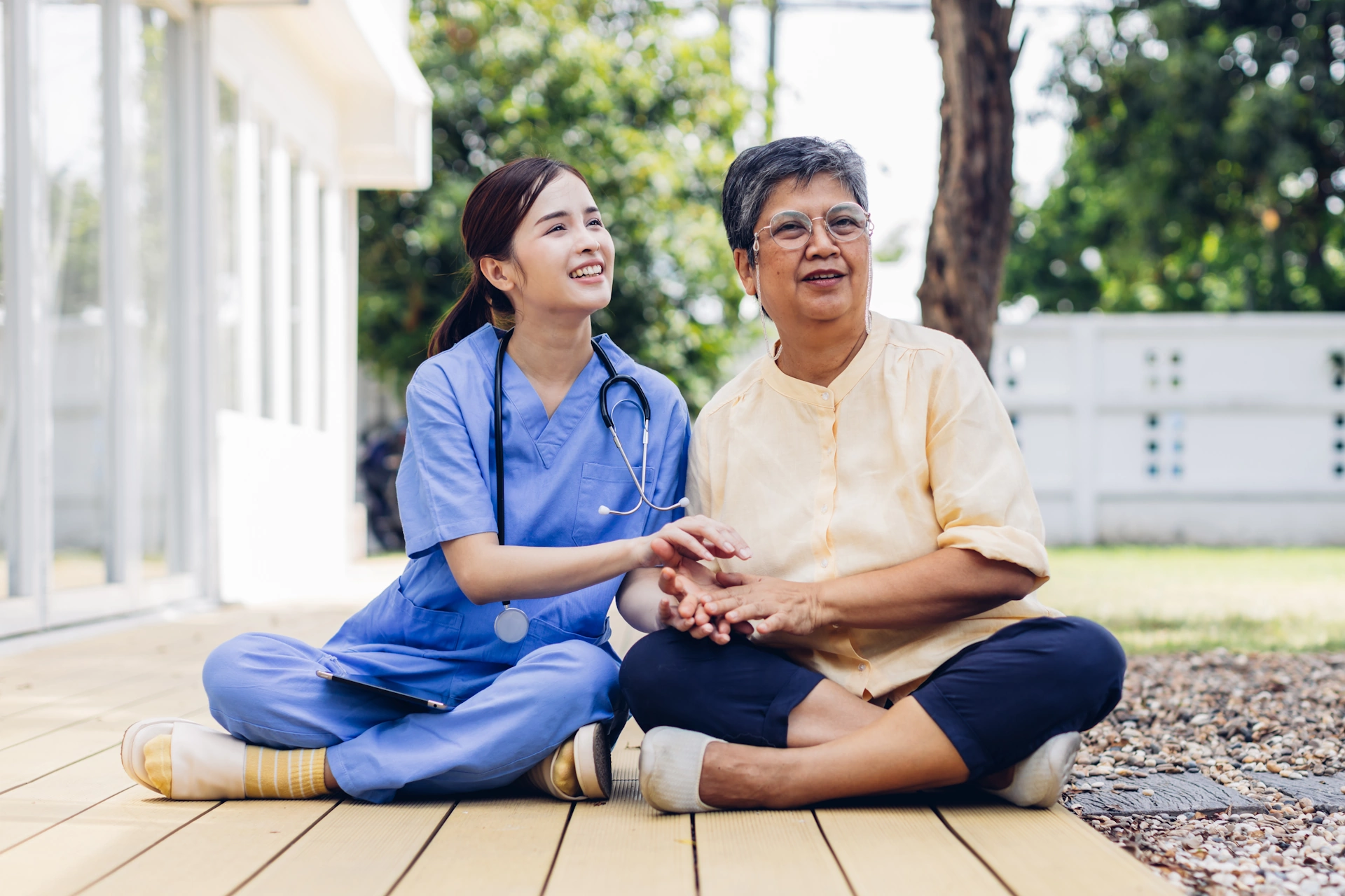 A compassionate nurse provides support and companionship to an older woman outdoors.